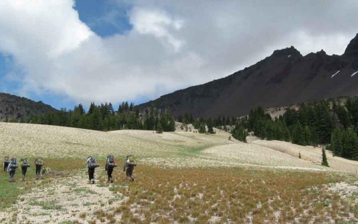 a group of backpacking students hike across a grassy alpine meadow on an expedition in oregon